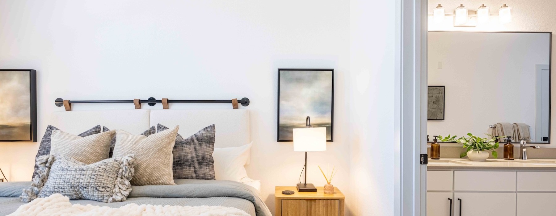 a model bedroom with a bed and a view of the bathroom with a large mirror